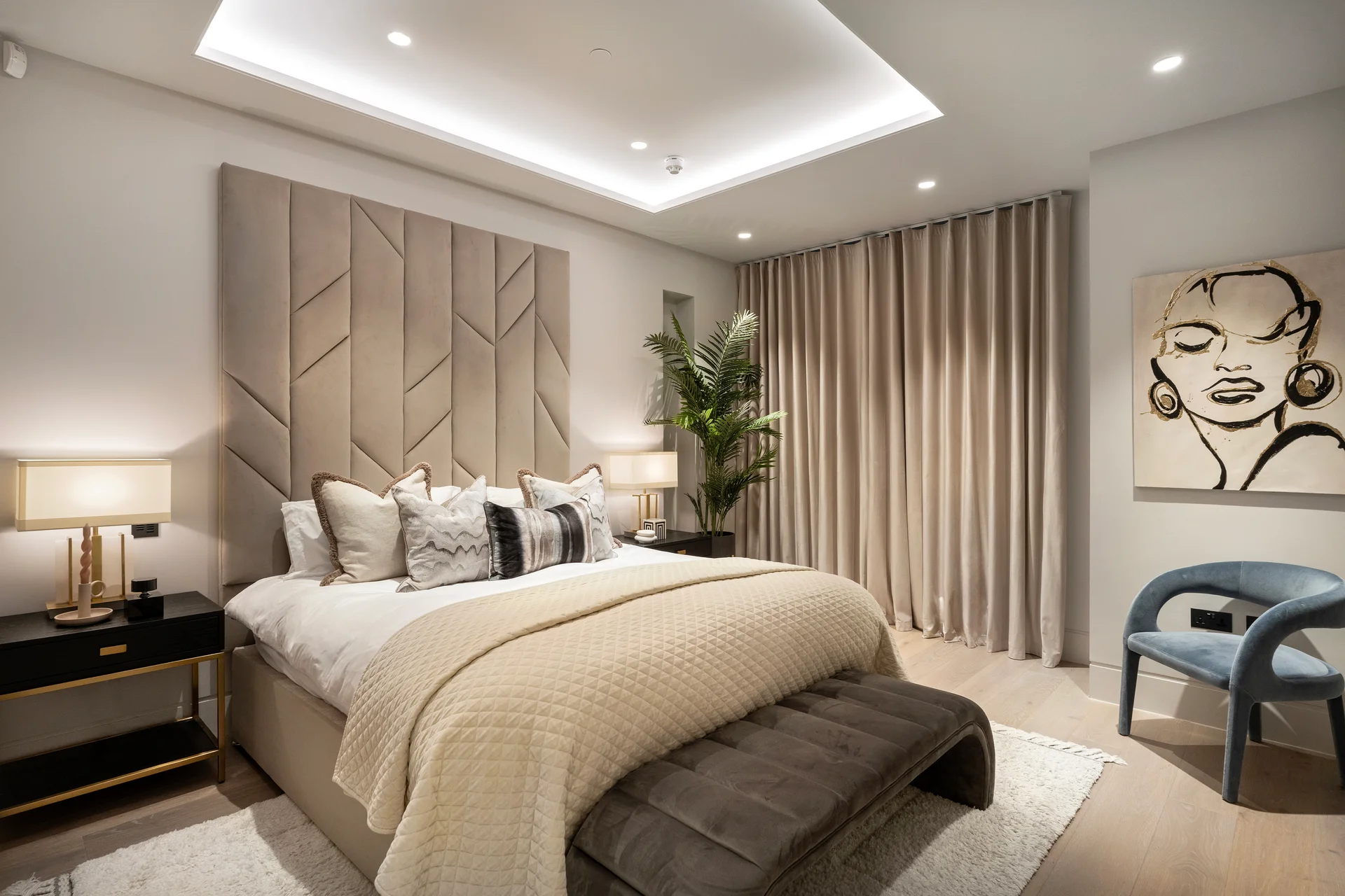 Modern bedroom with a stylish bed, decorative pillows, curtains, a plant, and artwork on the wall.