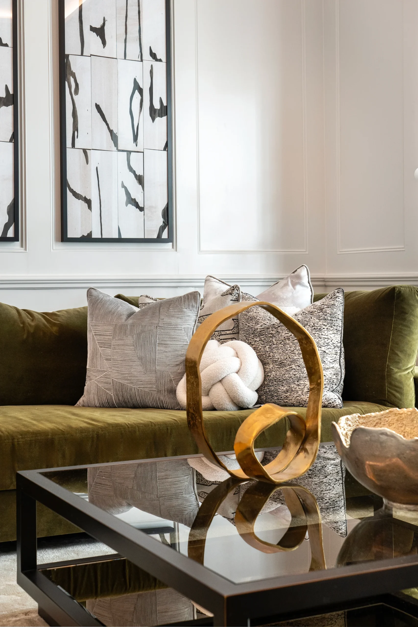 A modern living room featuring a green sofa, decorative pillows, a glass coffee table, and abstract artwork on the wall.