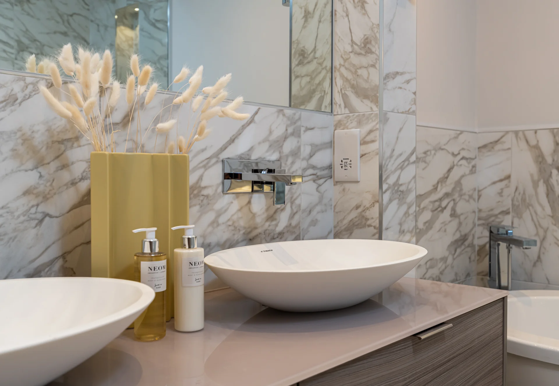Stylish bathroom featuring marble walls, two sinks, and a decorative vase with dried flowers.