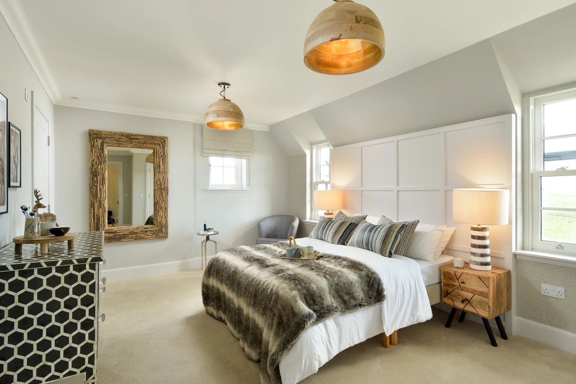 Cozy bedroom featuring a large bed, decorative pillows, stylish lamps, and a contemporary wall mirror.