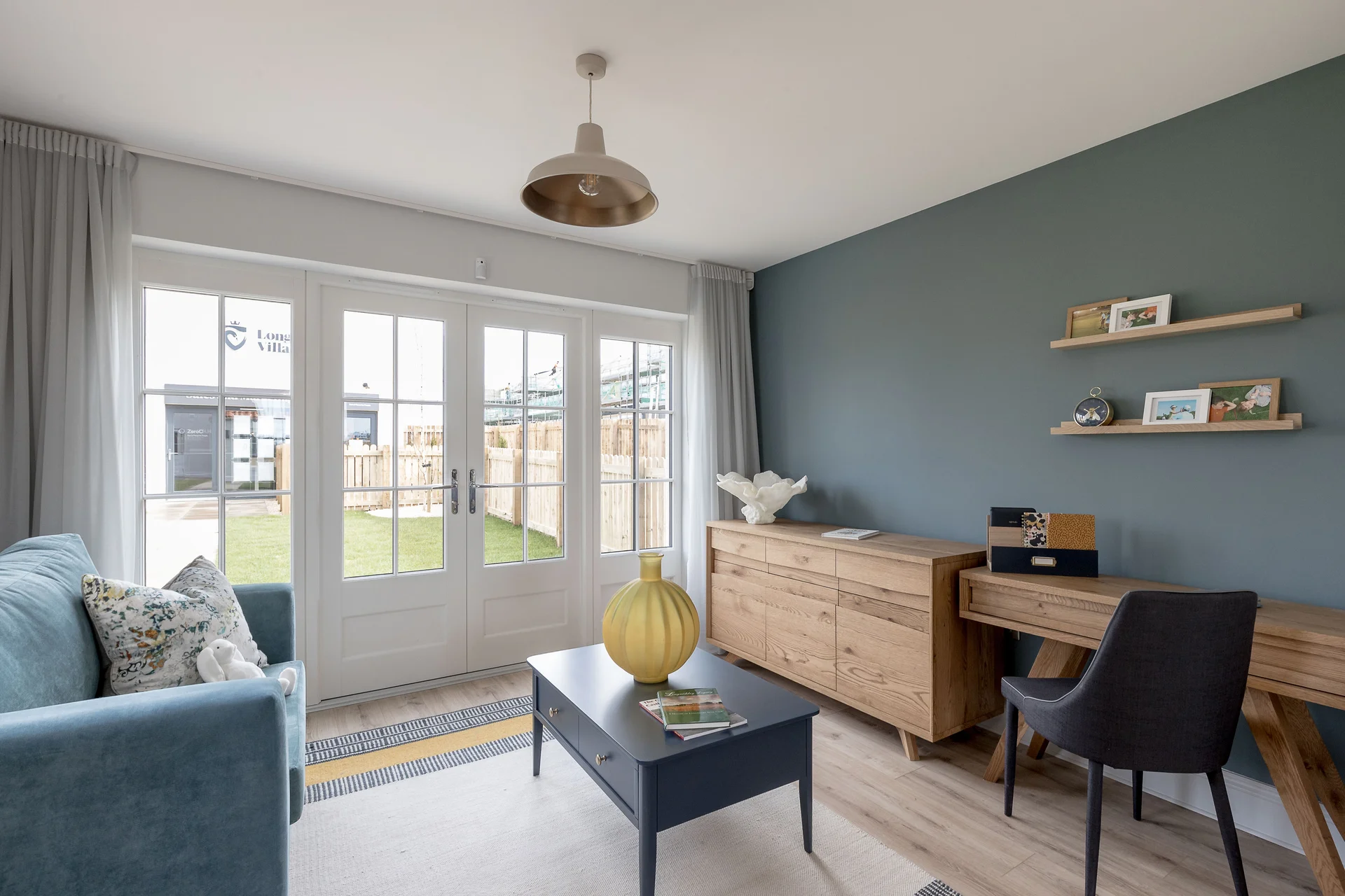 Living room with a blue sofa, wooden desk, decorative yellow lamp, and patio doors leading to an outdoor space.