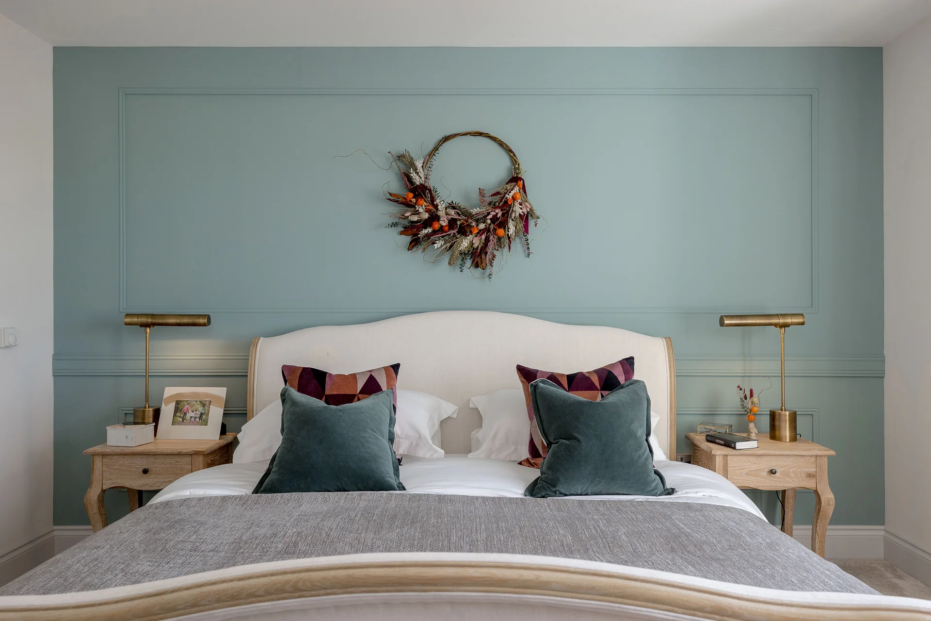 Cozy bedroom featuring a light green accent wall, a decorative wreath, and a bed with plush pillows and bedside lamps.