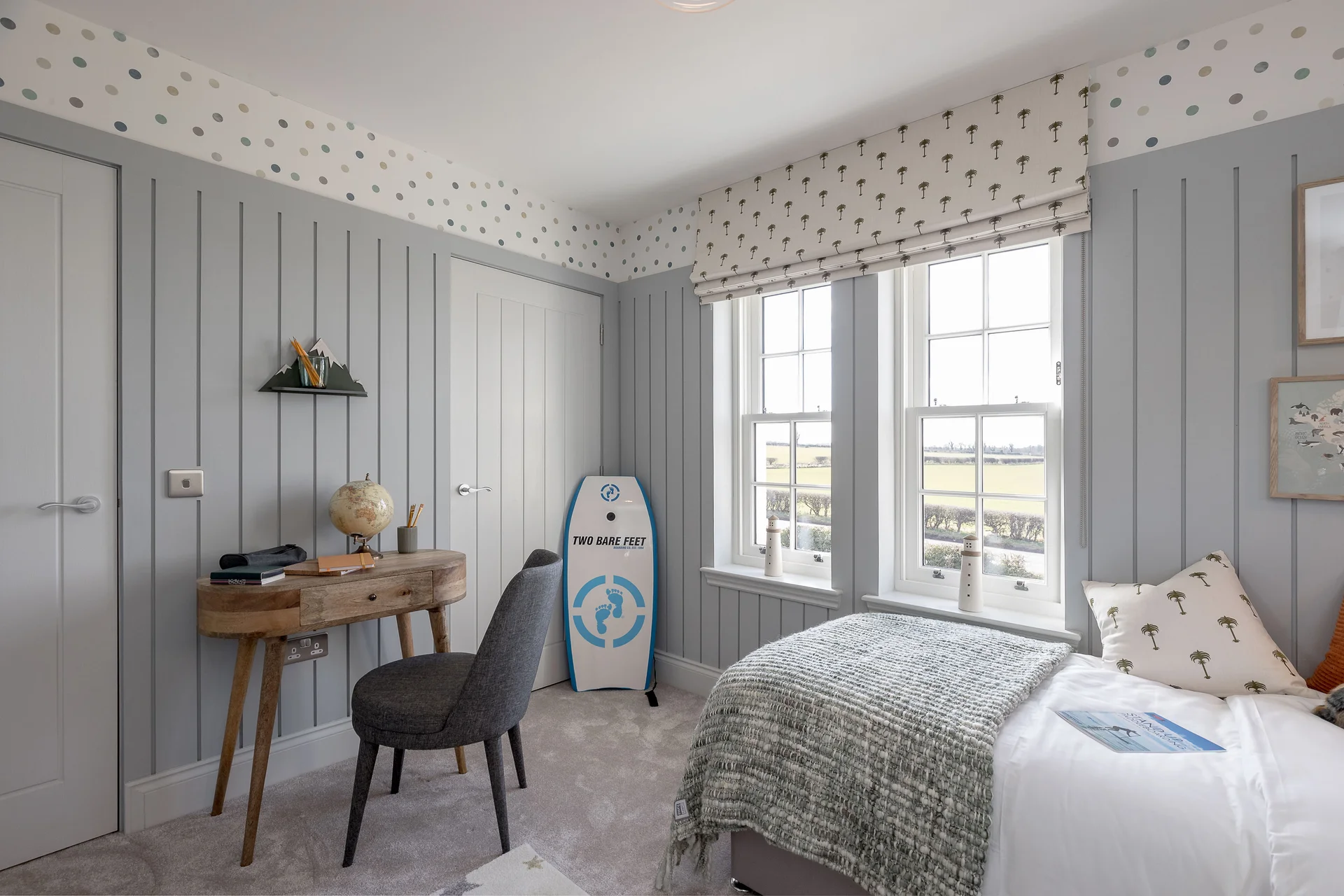 Cozy bedroom with gray paneling, a wooden desk, a surfboard, and large windows providing natural light.