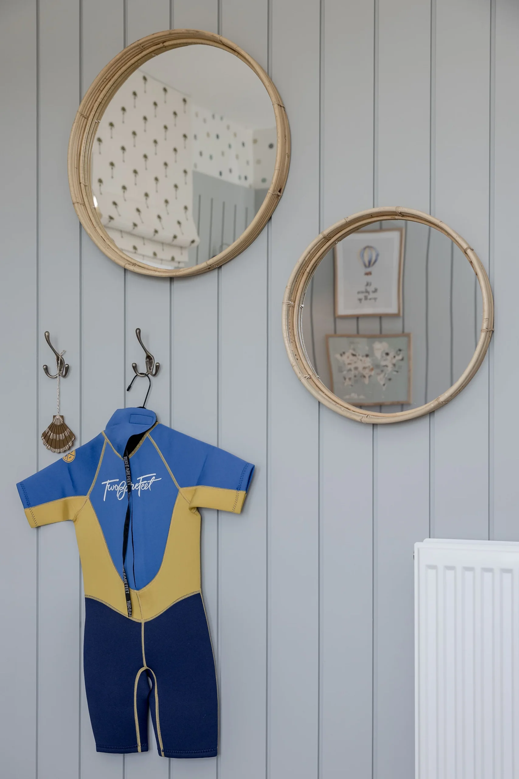 A blue and yellow wetsuit hangs on hooks against a wooden wall, flanked by two round mirrors.