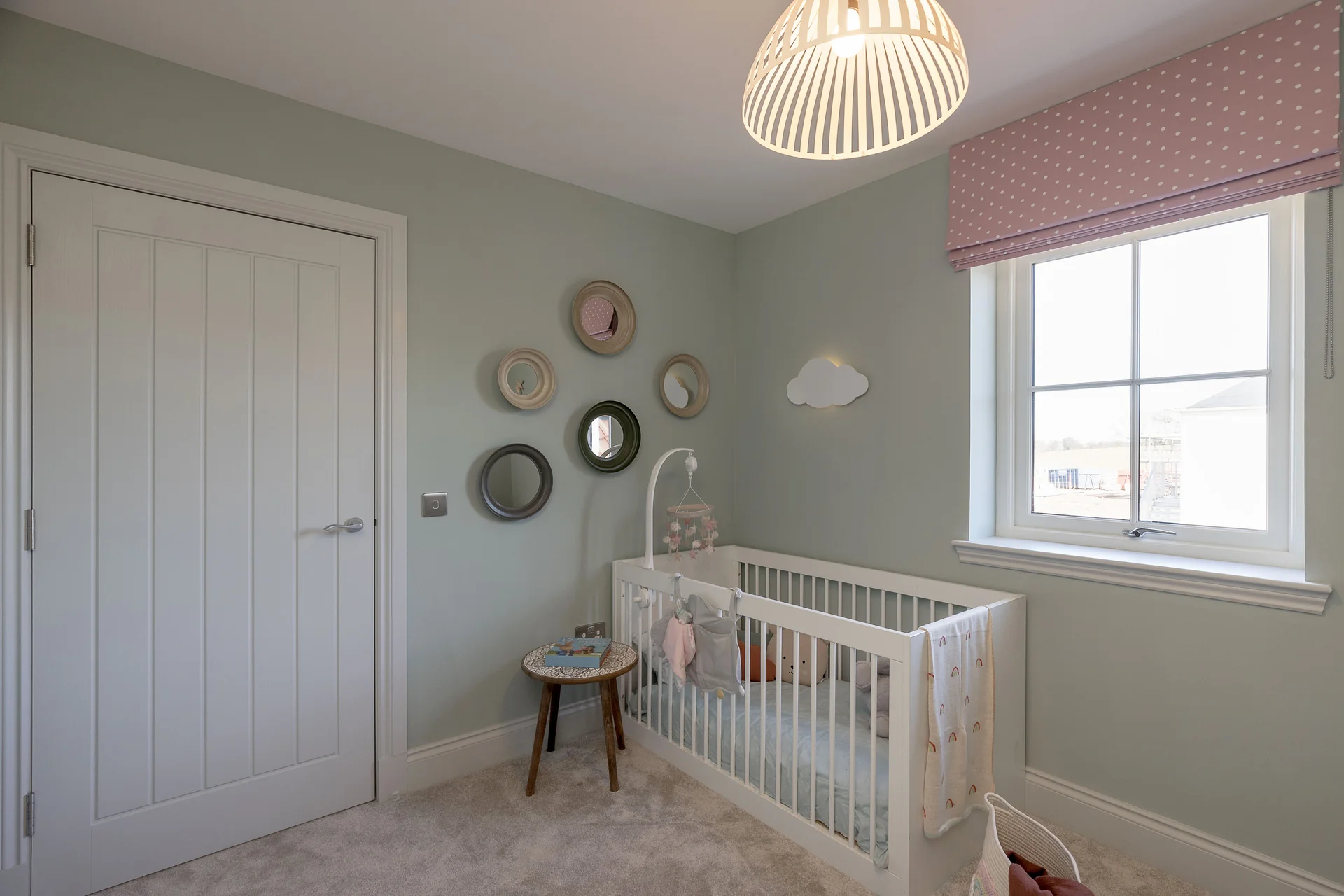 Brightly lit nursery with a crib, decorative wall mirrors, and a small side table. Soft color palette and cozy decor.