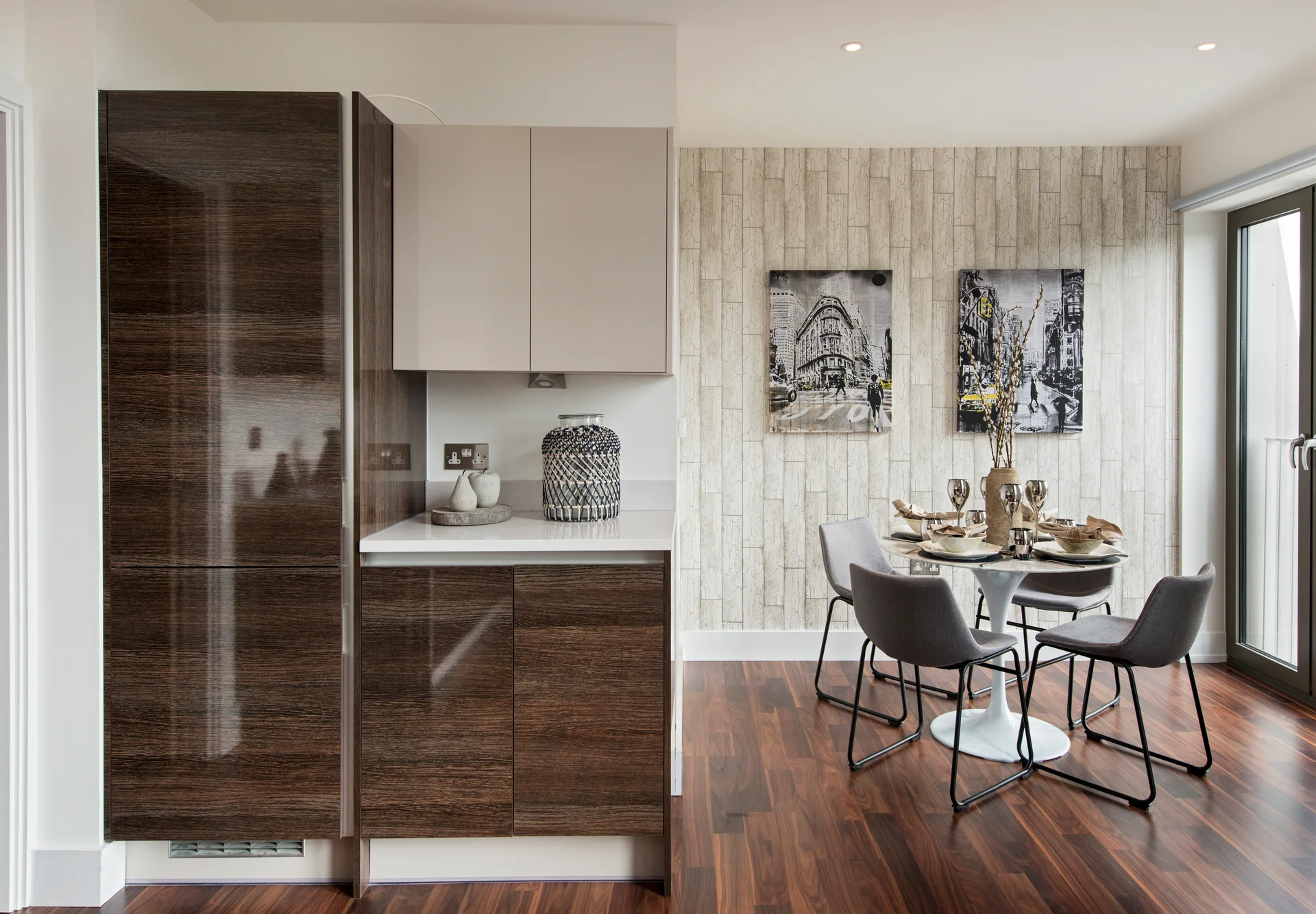 Modern kitchen area featuring dark wood cabinets, a dining table set for four, and wall art in a bright, minimalist space.
