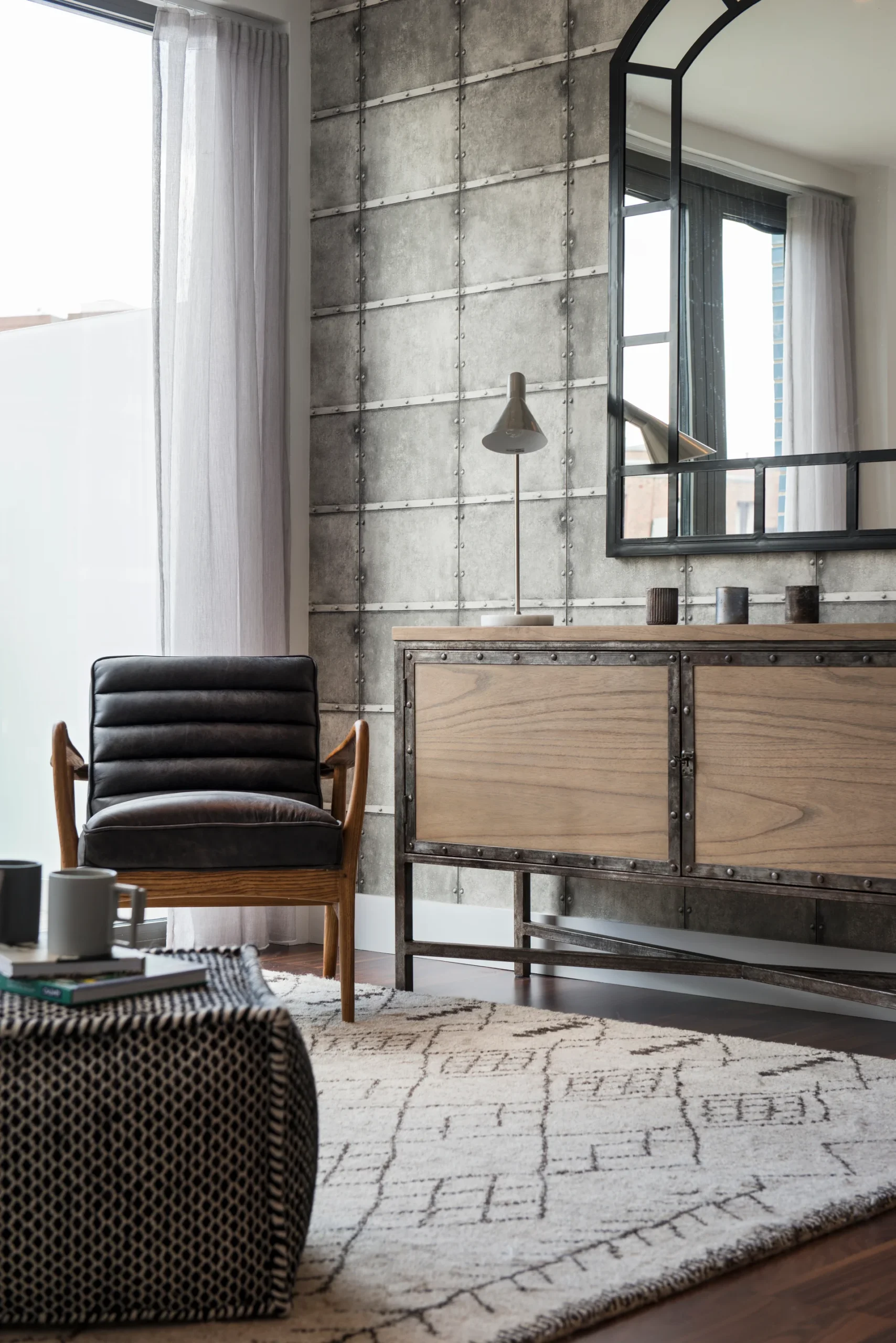Modern living room featuring a black chair, wood sideboard, round table, and textured rug against a concrete wall.