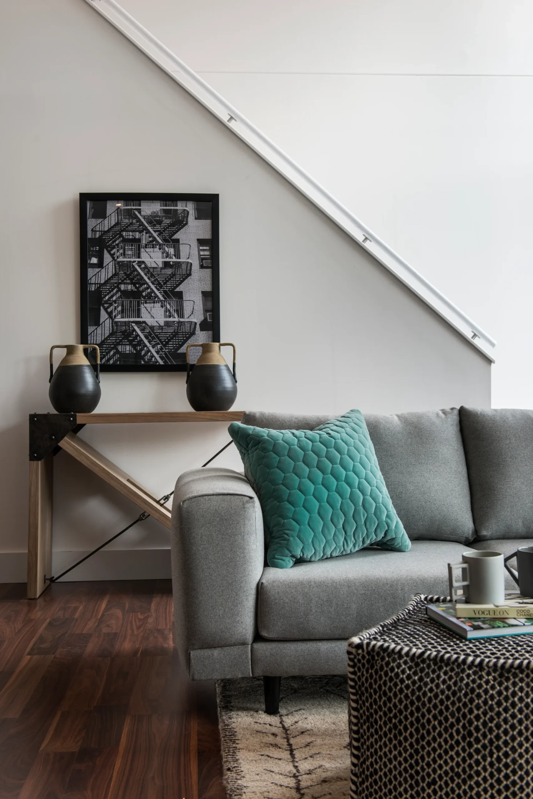 Modern living room with a gray sofa, teal pillow, geometric artwork, and stylish furniture against a light backdrop.
