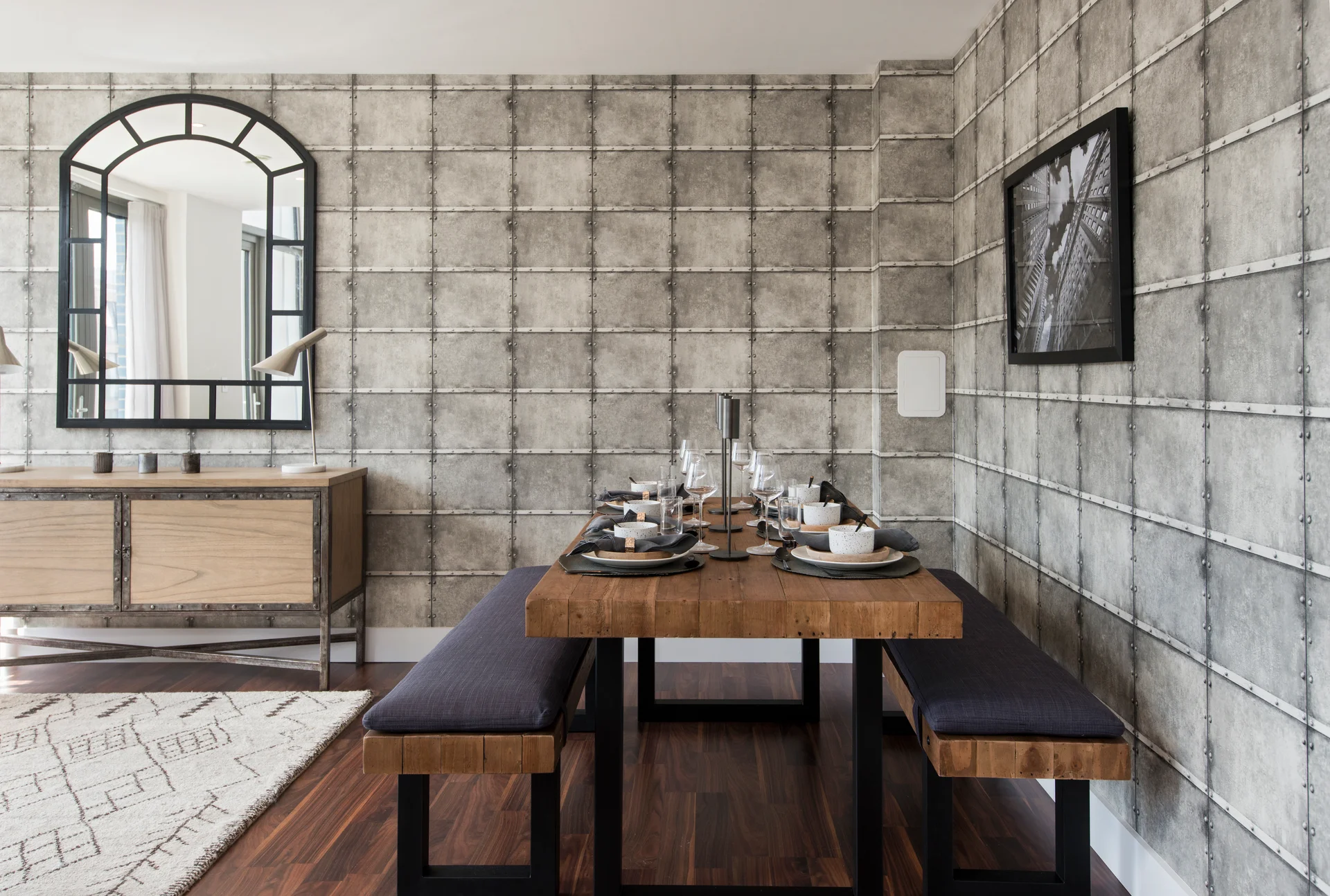 Stylish dining area featuring a wooden table with benches, modern decor, and a vintage mirror on a textured wall.