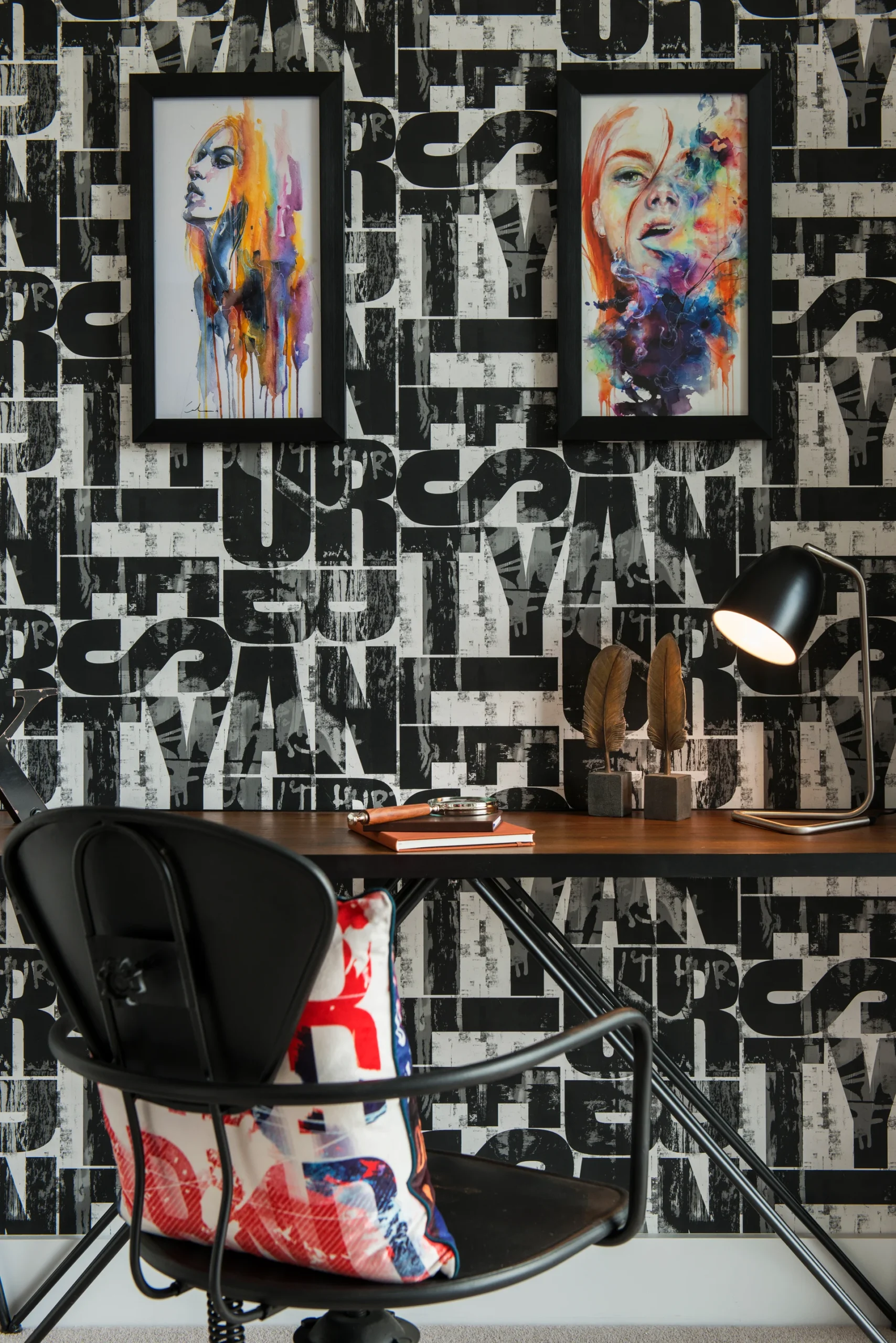 A stylish workspace featuring a wooden desk, black chair, and vibrant artwork on the bold patterned wallpaper.