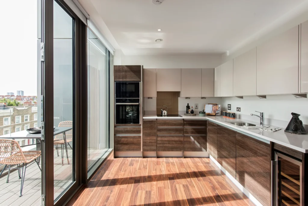 Modern kitchen with sleek cabinets, wooden flooring, large windows, and a balcony view.