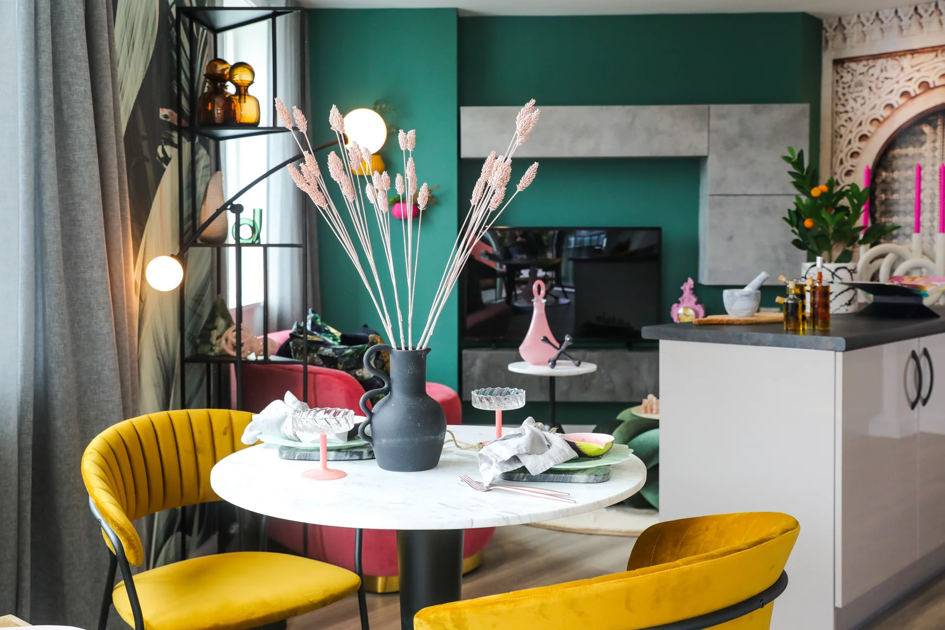 Bright dining area with a round table, yellow chairs, and a vase of decorative flowers against a green wall.