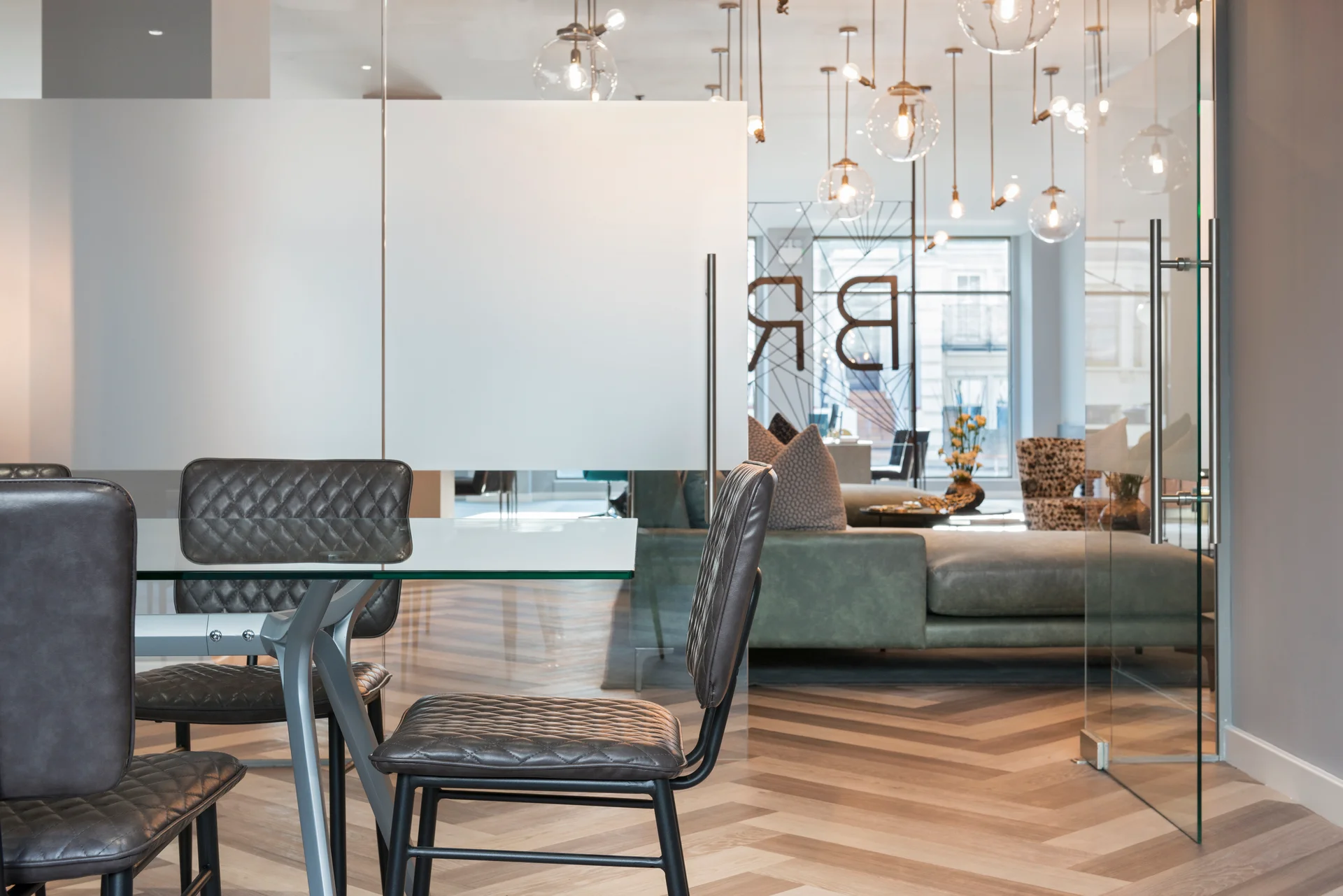 Modern dining area with glass table, stylish chairs, and a view of a bright, elegant living room beyond.