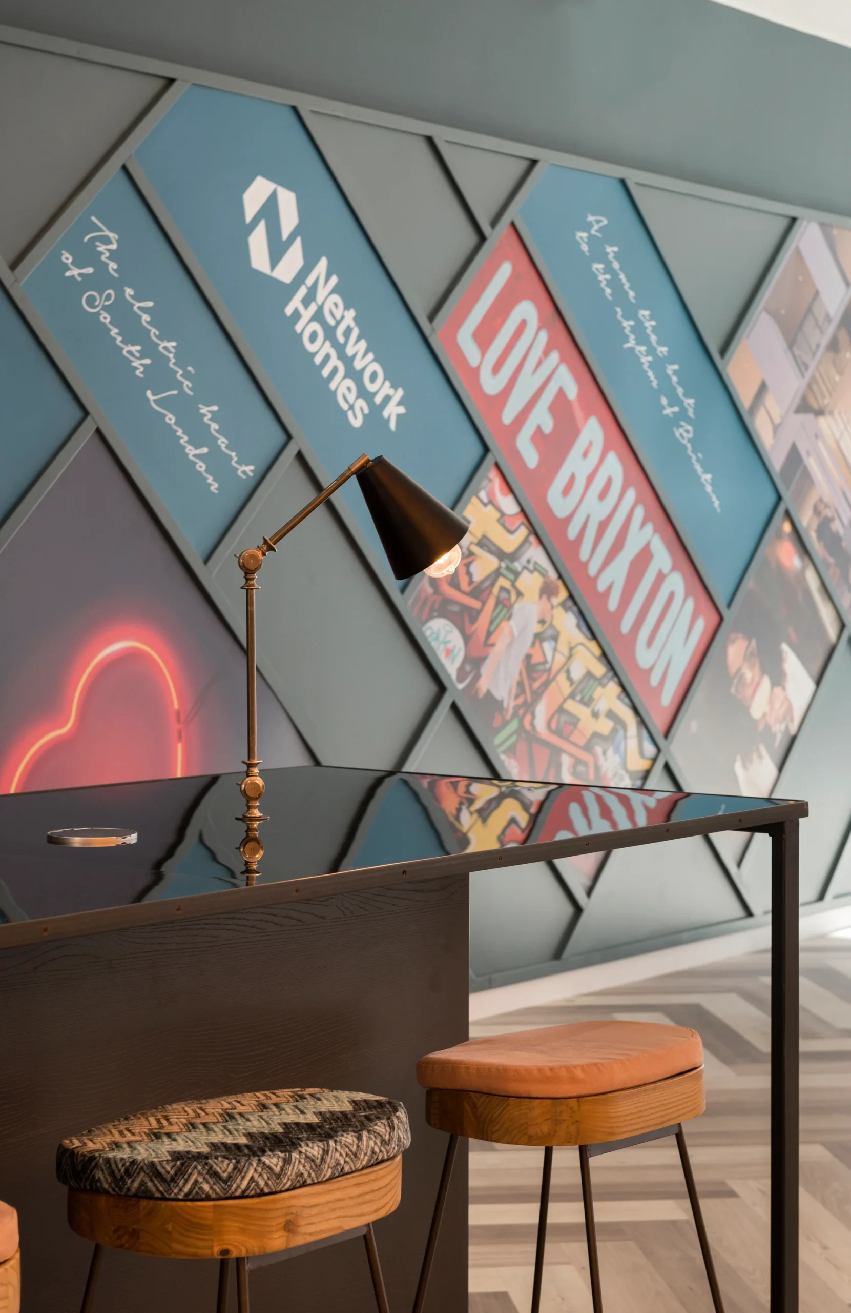 A modern bar area with stools, featuring a vibrant wall displaying various colorful signs and messages about Brixton.