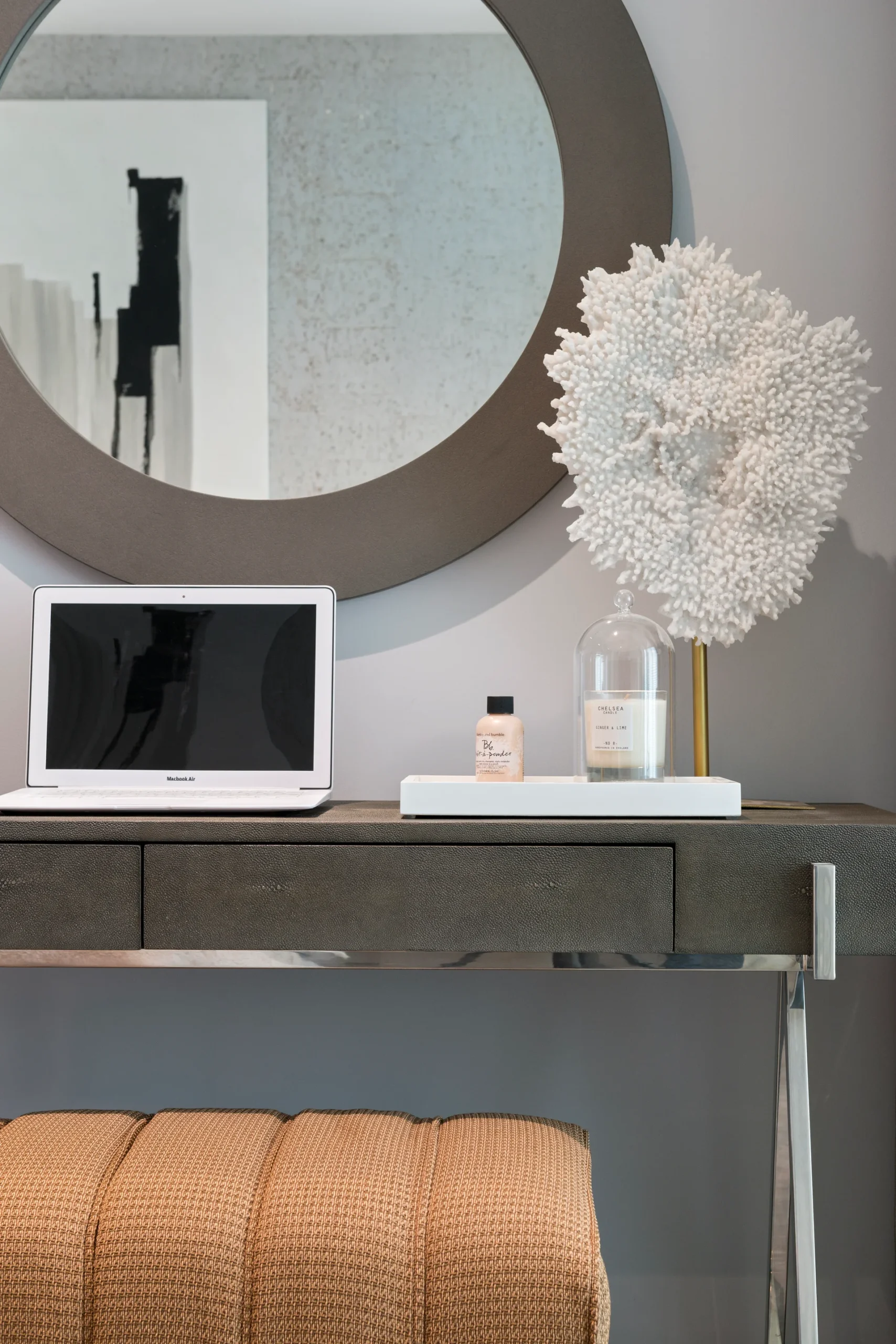 A minimalist desk with a laptop, decorative plant, and a round mirror above in a modern interior setting.