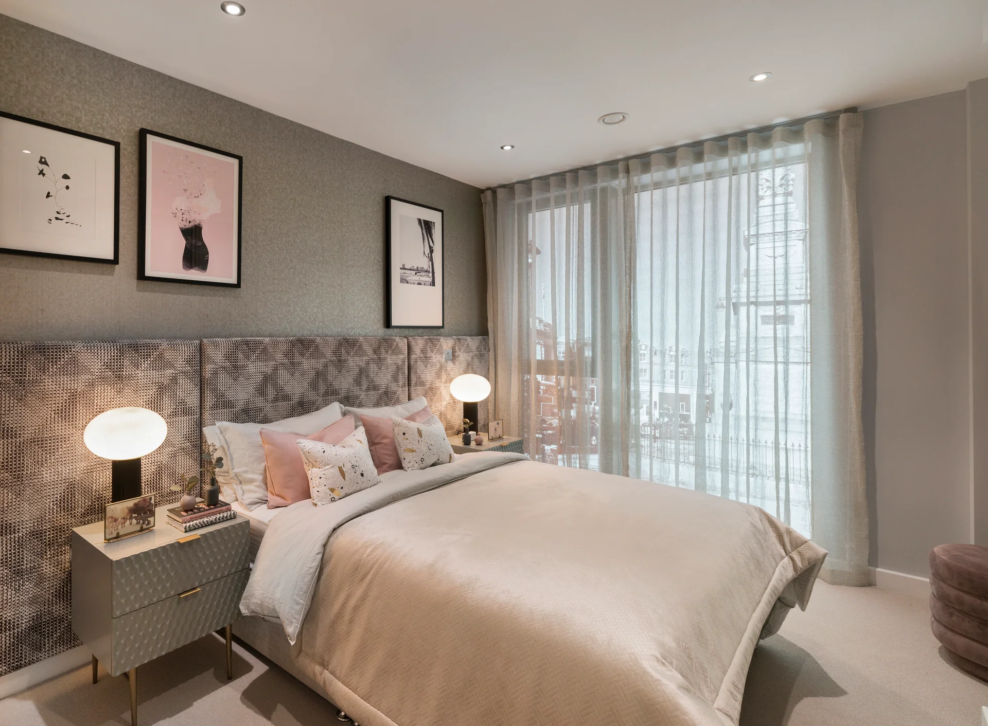 Stylish bedroom with gray walls, decorative artwork, a plush bed, and large windows covered with sheer curtains.