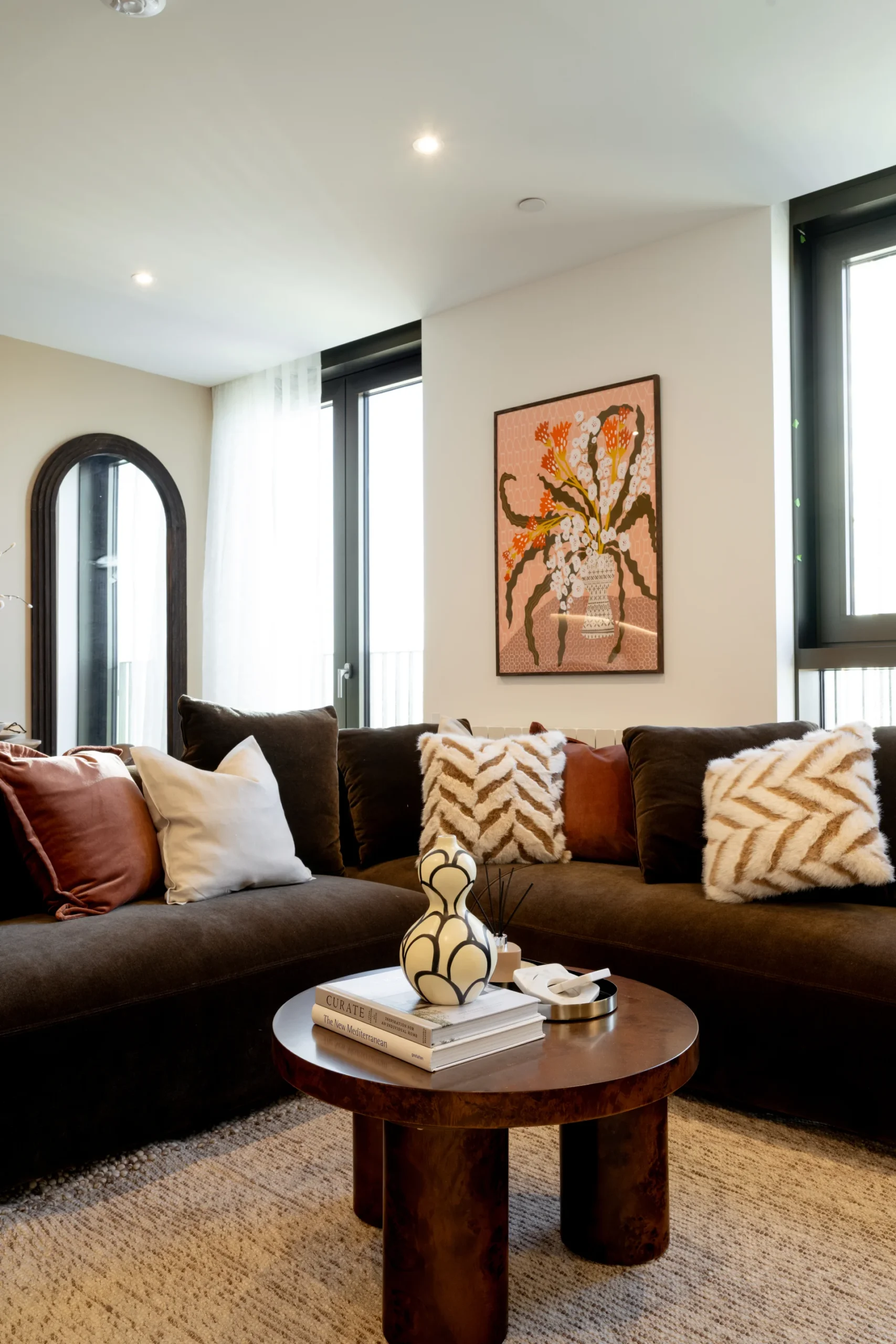 Modern living room featuring a dark couch with patterned pillows, coffee table, and wall art. Bright and stylish atmosphere.