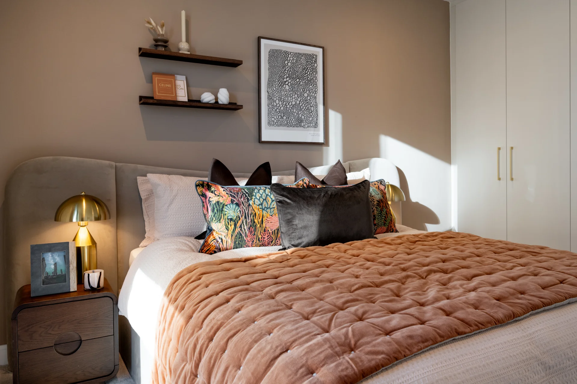 Cozy bedroom featuring a quilted blanket, decorative pillows, a nightstand with a table lamp, and wall art.