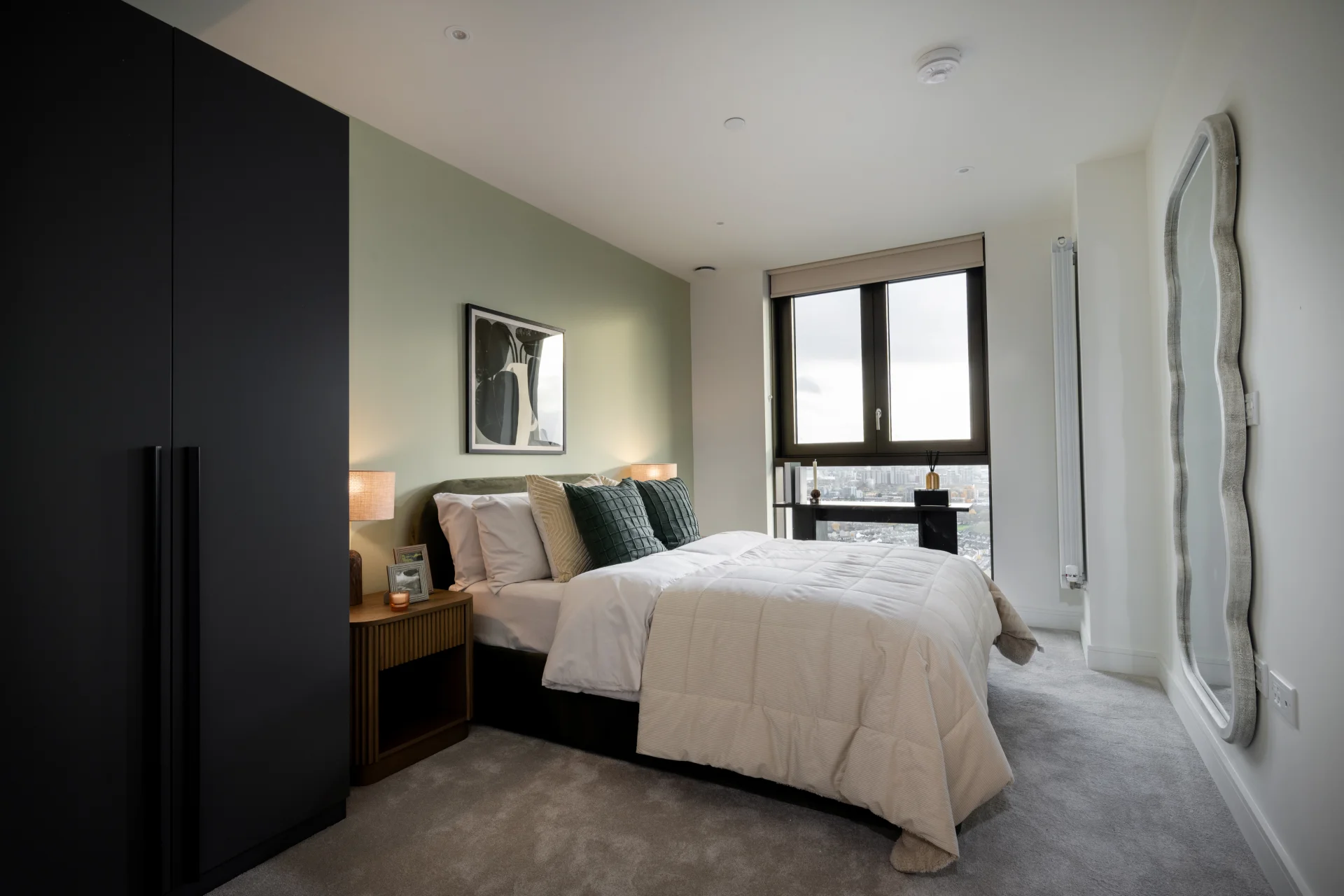 Modern bedroom with a green accent wall, a large window, and contemporary furnishings, including a cozy bed and stylish