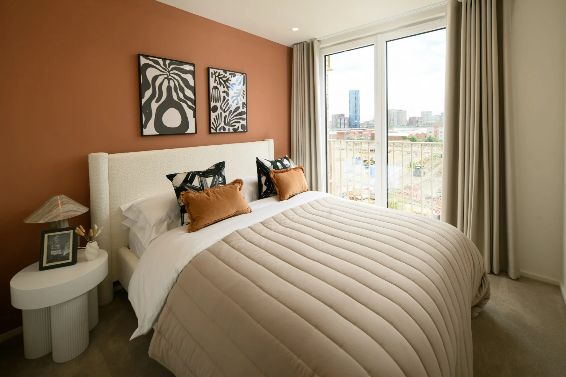 Stylishly furnished bedroom with a large bed, decorative pillows, and two framed artworks against an orange wall.