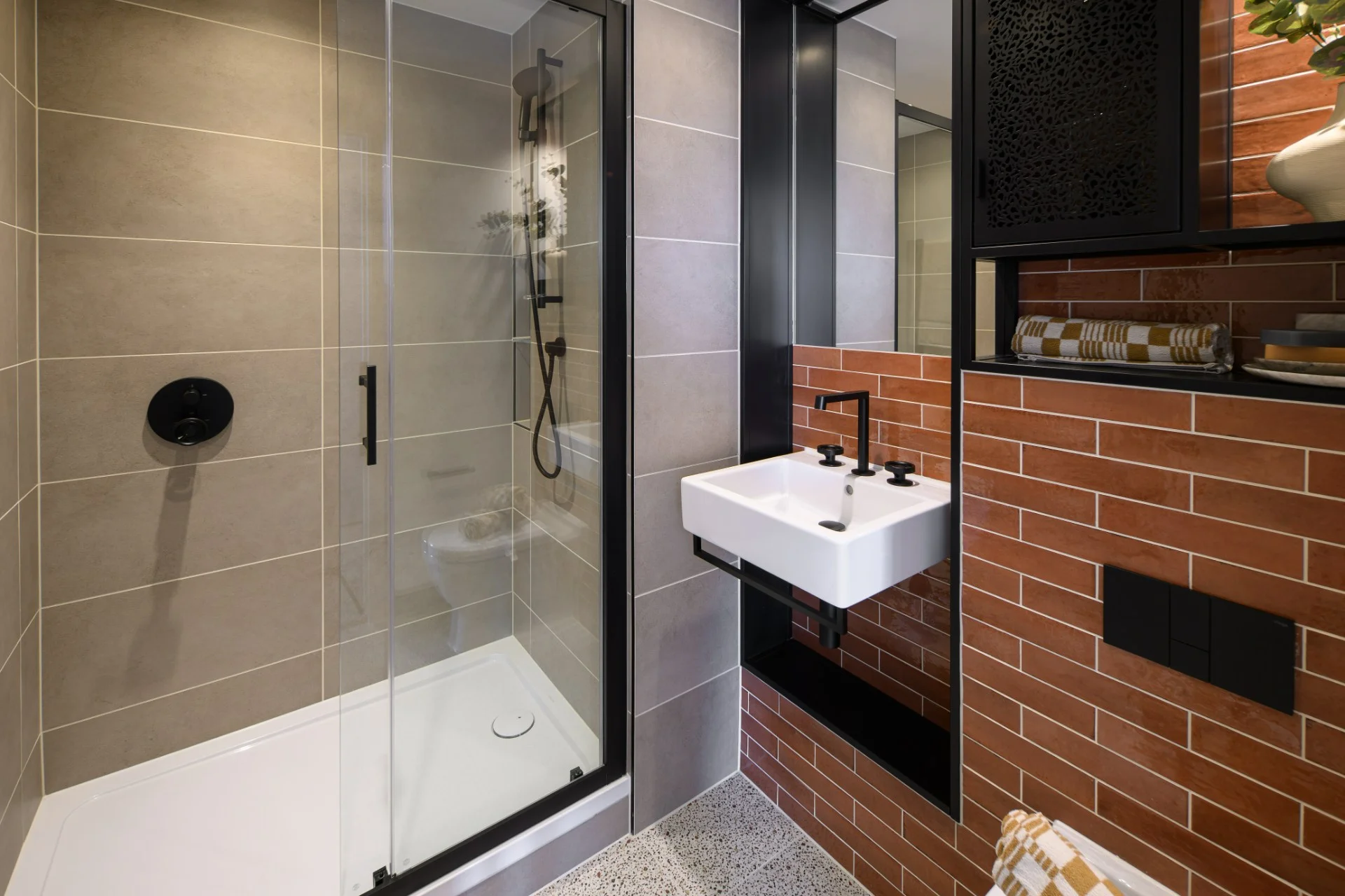 Modern bathroom featuring a glass shower, wall-mounted sink, and a mix of tile textures in neutral tones.