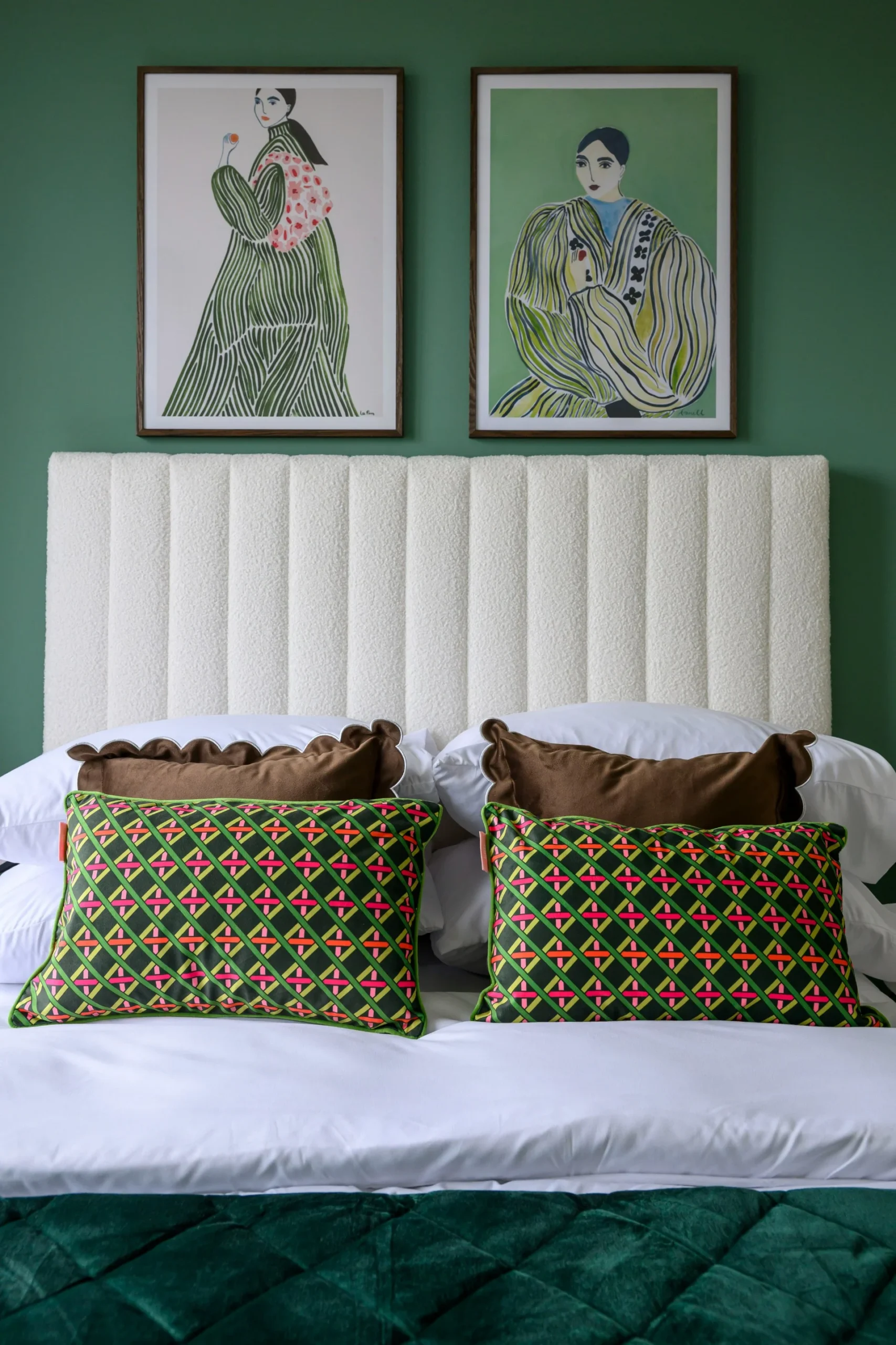 Stylish bedroom featuring a tufted headboard, patterned pillows, and framed artwork on a green wall.